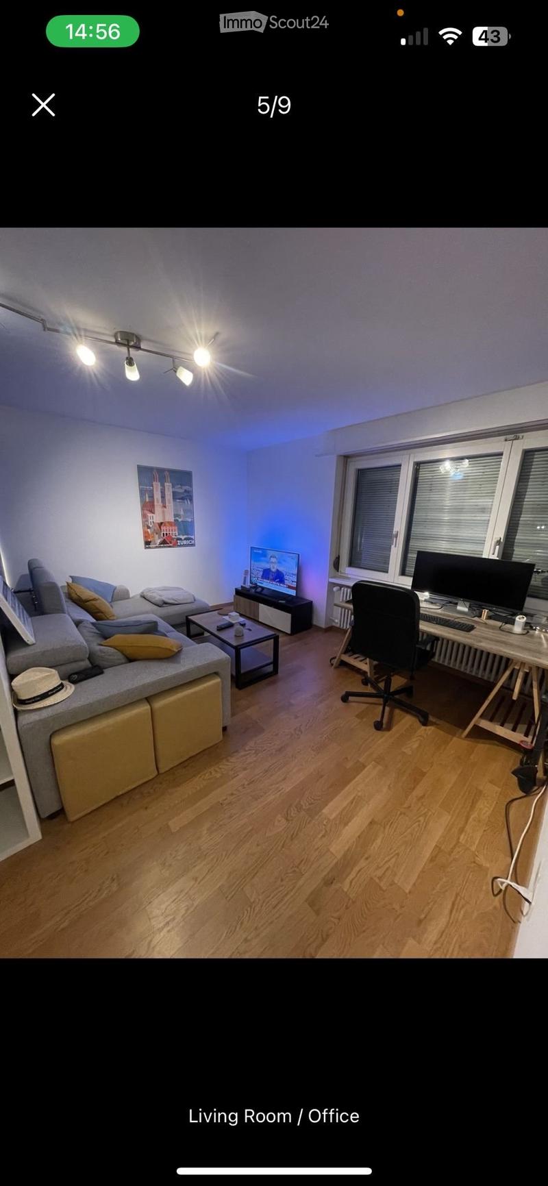 Living room with a grey sectional sofa, coffee table, TV, desk with computer, and a picture frame on the wall.
