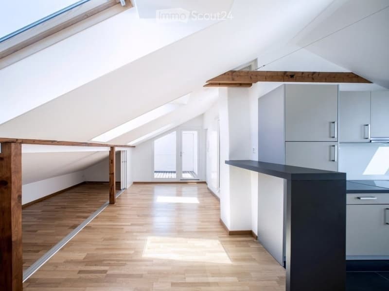 Bright, modern kitchen with light grey cabinets, dark countertop, and wooden flooring. Features large windows and a skylight, creating a spacious and airy atmosphere.