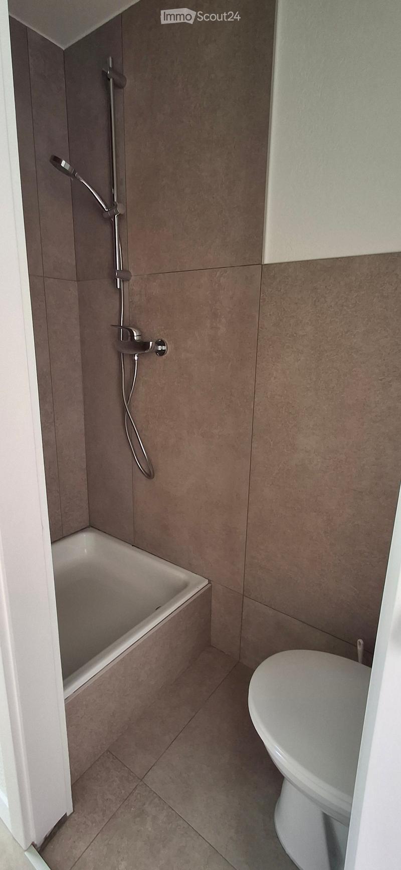 Modern bathroom with a bathtub, toilet, and a handheld showerhead attached to the wall.