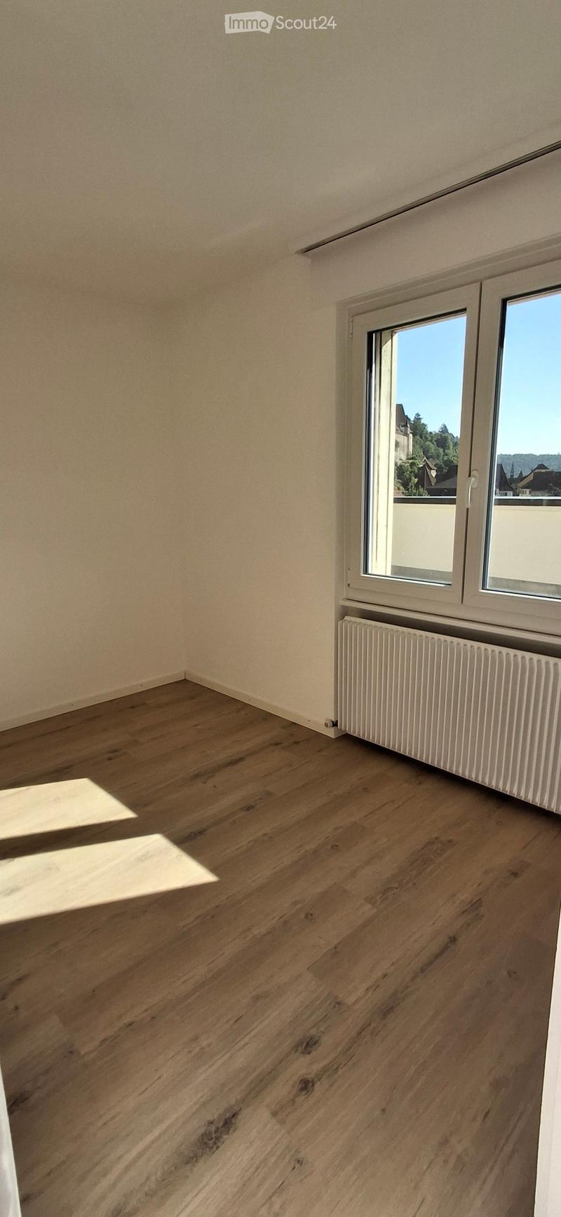 Empty room with wooden flooring, white walls, and a window with a radiator below it.