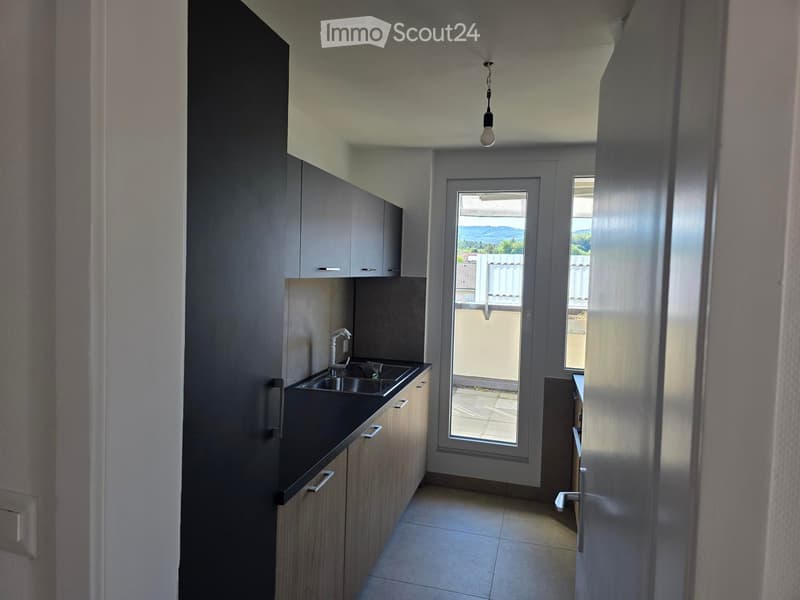 Modern kitchen with sleek cabinets, a black countertop, and a stainless steel sink. A large window offers a view of the outdoor area.