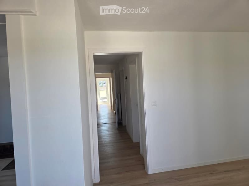 Empty hallway with white walls, wooden flooring, and multiple doors leading to other rooms.
