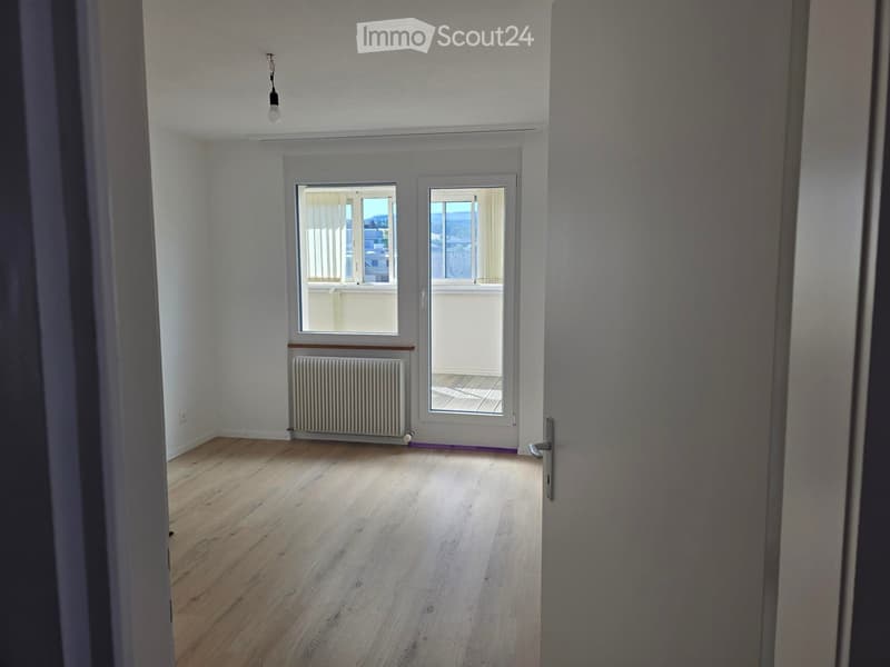 Empty room with wooden flooring, white walls, large windows, radiator, and a view of the outside area.