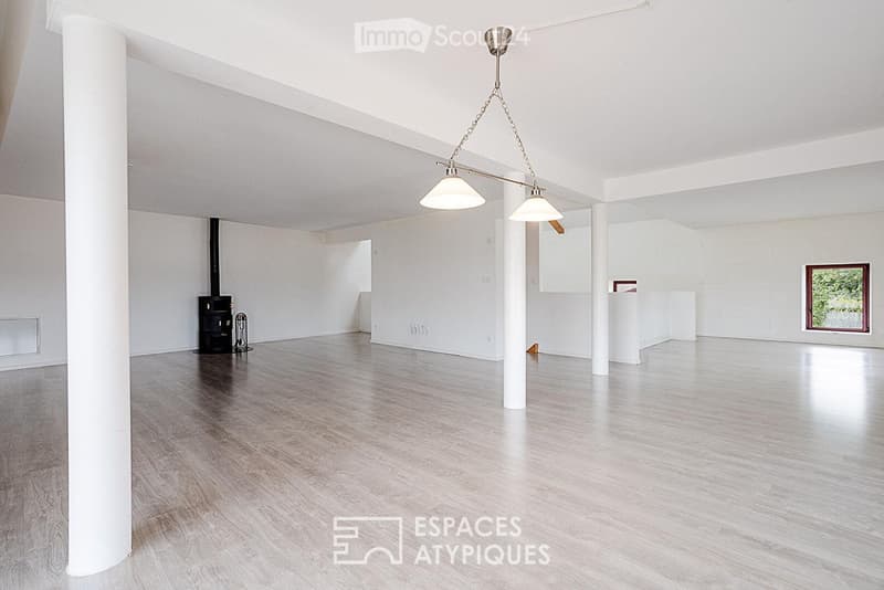 Empty room with white walls, wooden floor, white columns, and a hanging light fixture. A small black stove is visible in the corner.