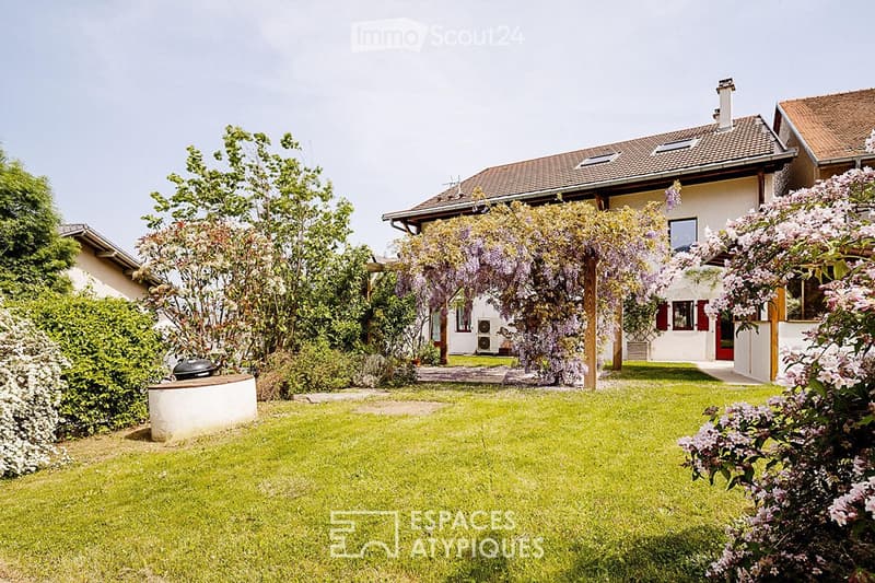 Well-maintained garden with green lawn, flowering shrubs, and a pergola covered with wisteria vines leading to a house entrance.