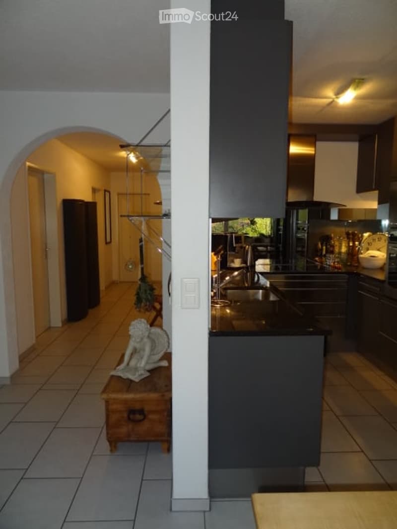 Modern kitchen with dark cabinets, a central island, and a sink. A small table with a statue sits in the adjacent hallway.