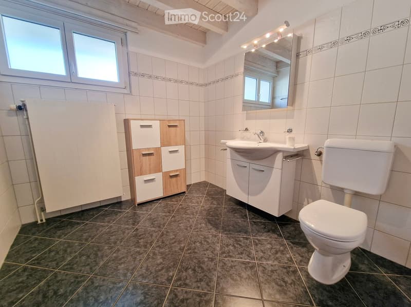Modern bathroom with white tiles, dark tiled floor, sink with cabinet, toilet, mirror with lighting, and storage unit.