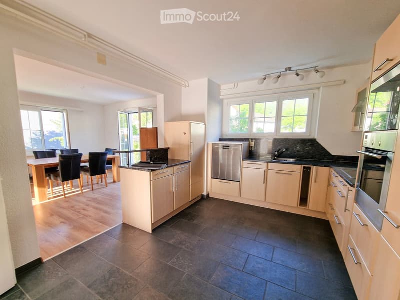 Modern kitchen with light-colored cabinets, stainless steel appliances, and a dining area with a wooden table and chairs.