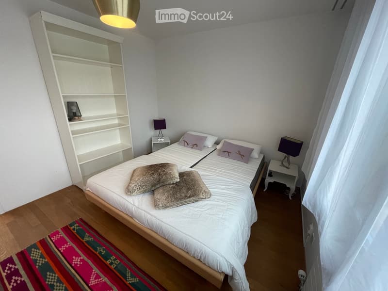 Cozy bedroom with a single bed, white bedding, two nightstands with lamps, a fur throw, and a colorful rug on the floor.