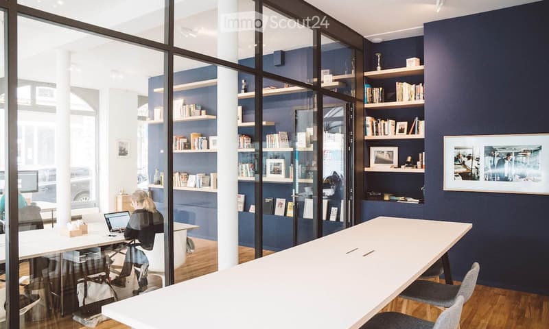 Modern office space with dark blue walls, white tables, chairs, shelves filled with books and decorative items, and a laptop on a desk.
