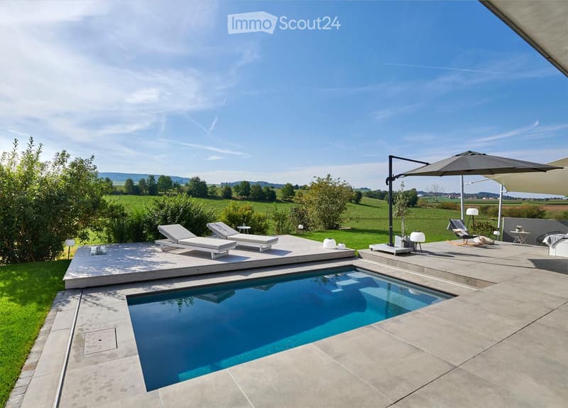 Outdoor patio with a swimming pool, sun loungers, umbrella, and surrounding greenery.