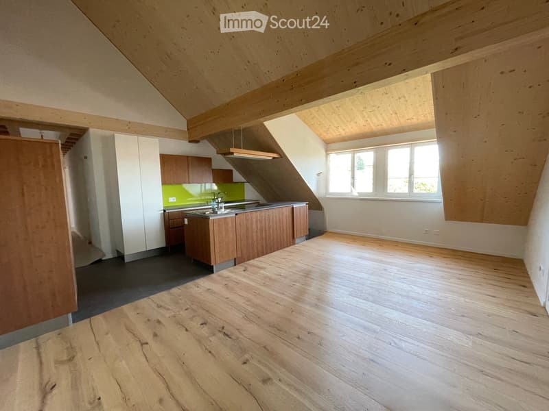 Modern kitchen with wooden cabinets, a stainless steel sink, and a green backsplash. The space features exposed wooden beams on the ceiling and large windows allowing natural light.