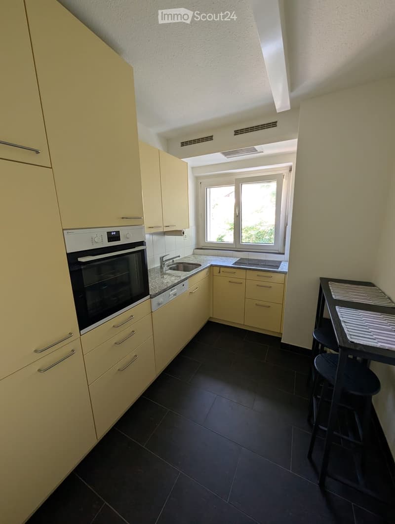 Modern kitchen with light-colored cabinets, granite countertop, black tiled floor, and a small dining area with a table and stools.
