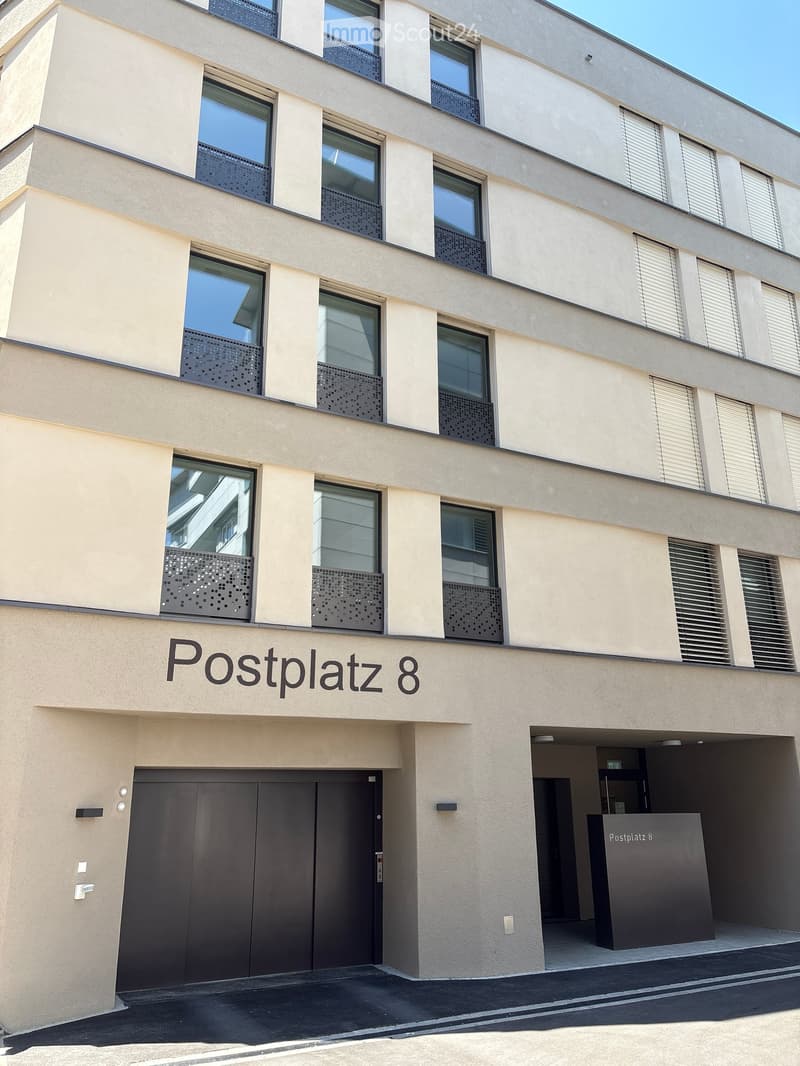 Modern multi-story building with large windows, decorative metal balustrades, and a prominent entrance labeled "Postplatz 8".