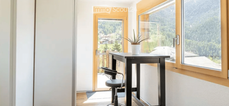 small room with a desk, chair, and a plant, large windows with a view of the mountains