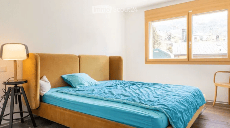 A bedroom with a bed, a lamp, a chair, and a window with a view of the outside