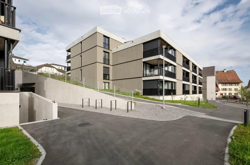 Modern apartment building with balconies, concrete driveway, landscaped area