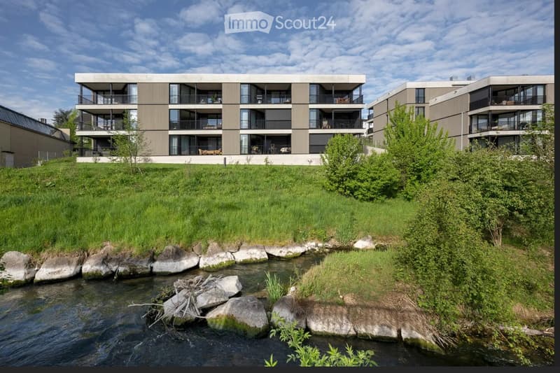 Modern apartment building with multiple floors, balconies, and a grassy area in front