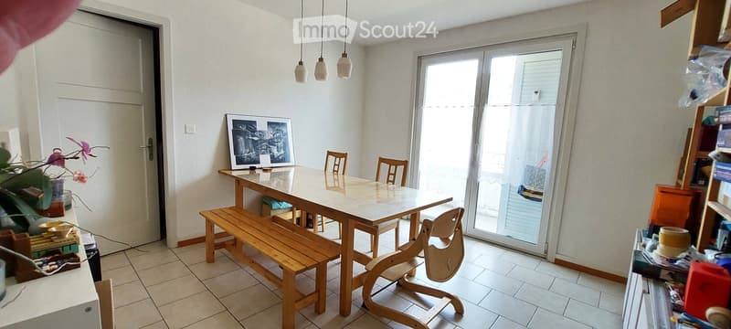 Dining room with a marble dining table, wooden chairs, a bench, and a picture frame on the wall. A sliding glass door leads to a balcony.