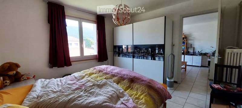 Cozy bedroom with a large bed, colorful bedding, a teddy bear on the bed, a modern wardrobe with a cityscape design, and a hanging lamp.