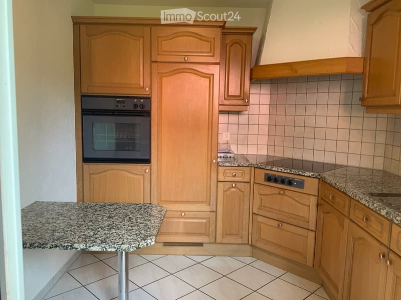 A modern kitchen with light wooden cabinets, granite countertops, and built-in appliances including an oven and stove.