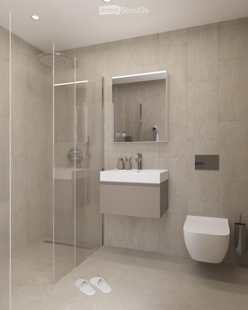 Modern bathroom with beige tiles, a white sink with a cabinet, a large mirror, a shower with a glass enclosure, and a toilet. The floor is tiled, and there are two white slippers placed near the shower area.