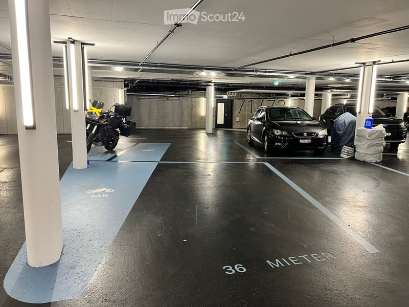 Underground parking area with marked spaces for cars and motorcycles, concrete pillars, and overhead lighting.