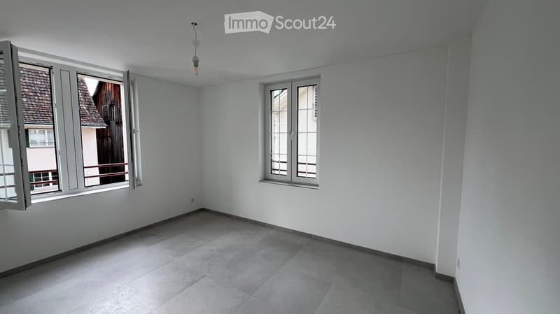 Empty room with white walls, tiled floor, and large windows with shutters. No furniture or equipment present.