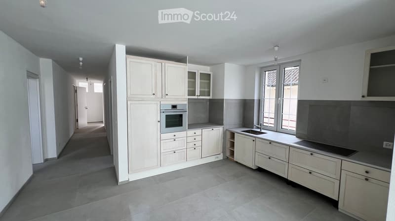 Modern kitchen with white cabinets, stainless steel oven, sink, and countertop. Large windows provide natural light.