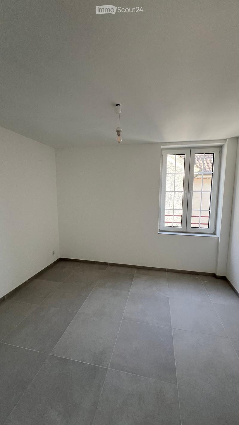 Empty room with grey tiled floor and white walls, featuring a single window with white frame and a hanging light fixture.