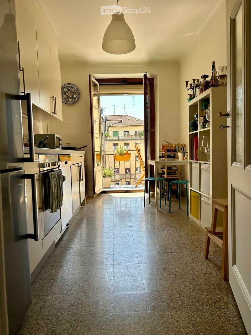 Modern kitchen with white cabinets, stainless steel appliances, and a small dining area leading to a balcony.
