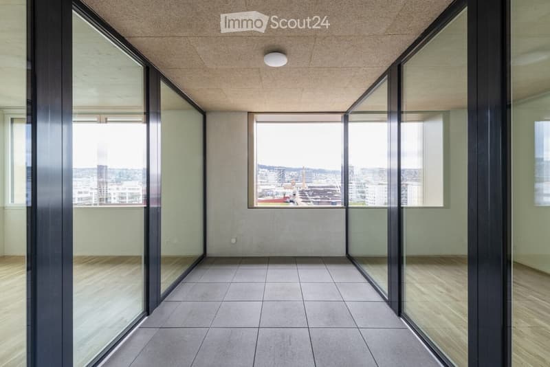 Empty room with large glass walls and a view of the cityscape, featuring a tiled floor and recessed lighting.