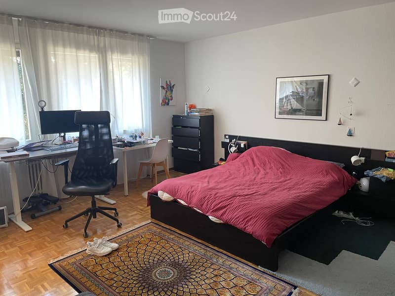 Well-lit bedroom with a double bed, desk, chair, and nightstand. Features a patterned rug, artwork, and a modern aesthetic.