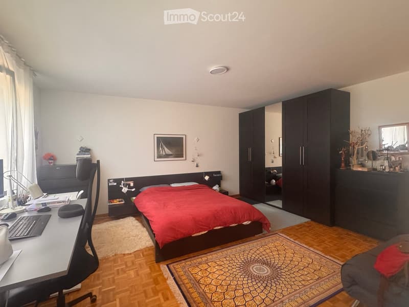 Modern bedroom with a double bed, desk, chair, wardrobe, and a small seating area with a sofa and rug.