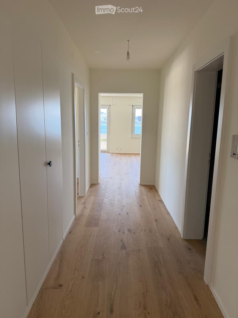 Empty hallway with light wooden flooring, white walls, and several doors leading to other rooms.
