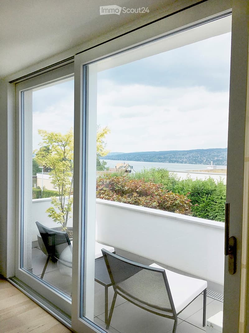 Balcony with a view of the water and surrounding greenery, featuring a single chair.