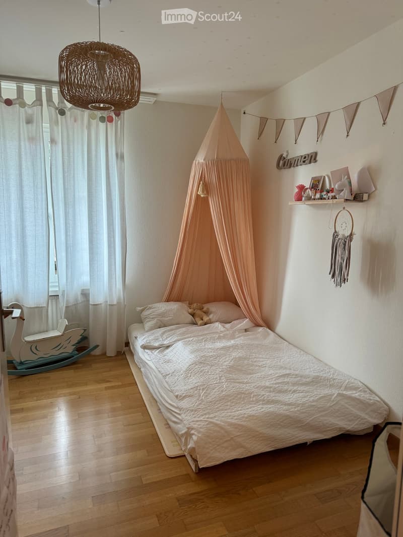 Cozy children's bedroom with a single bed, a rocking horse, a dreamcatcher, and a shelf with decorative items.