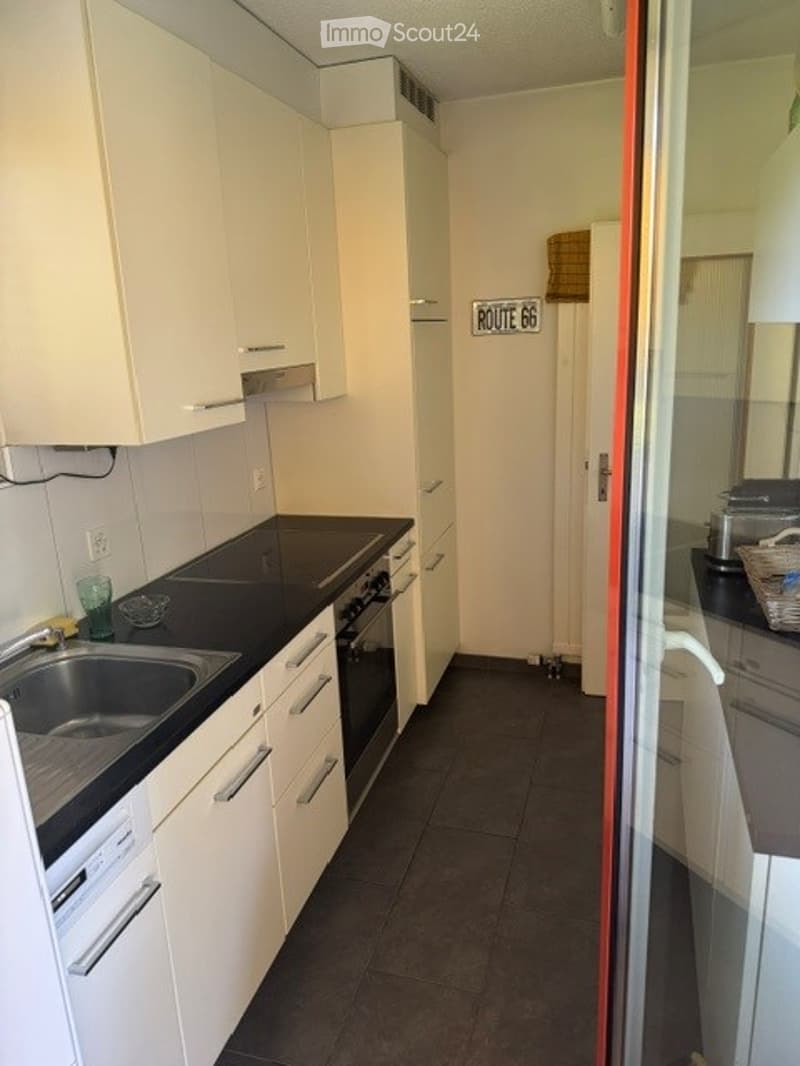 Modern kitchen with white cabinets, black countertop, stainless steel sink, and built-in oven. Includes a small basket on the counter and a decorative sign on the wall.