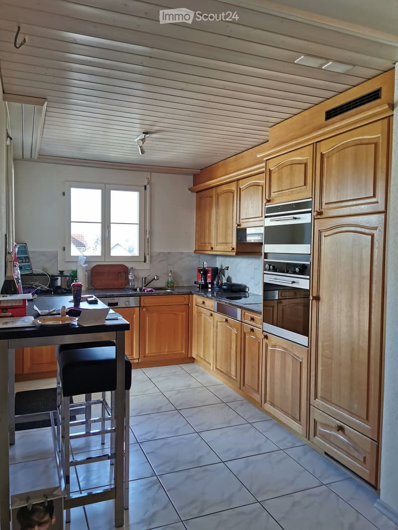 Bright kitchen with wooden cabinets, stainless steel appliances, a central island with a stool, and a window offering a view.