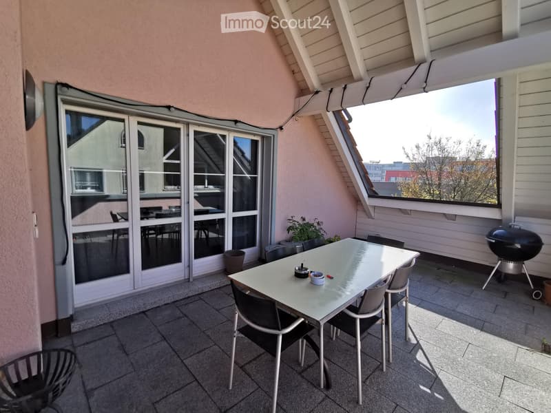 Balcony with a dining table, chairs, and a grill, featuring large windows and a view of the city.