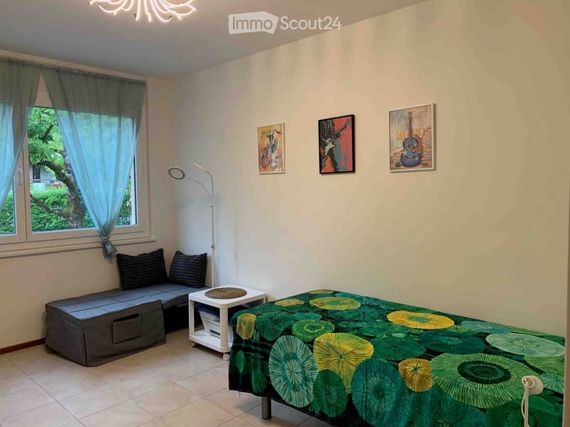 Cozy bedroom with a bed, sofa, small table, floor lamp, and artwork on the walls.