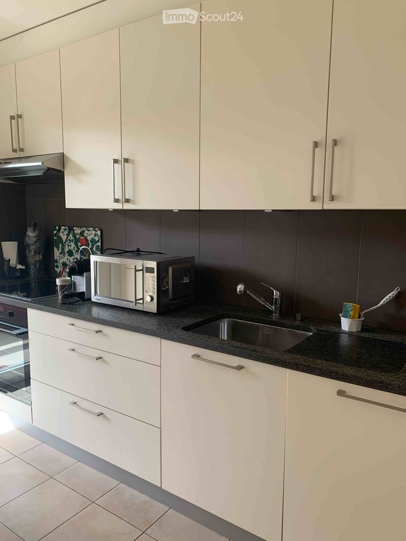 Modern kitchen with white cabinets, granite countertop, stainless steel microwave, sink, and faucet.