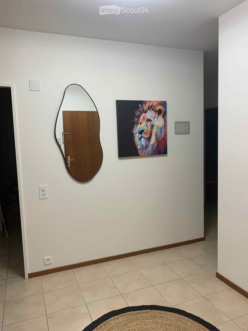Empty hallway with white walls, tiled floor, a large mirror, and a colorful lion painting on the wall.