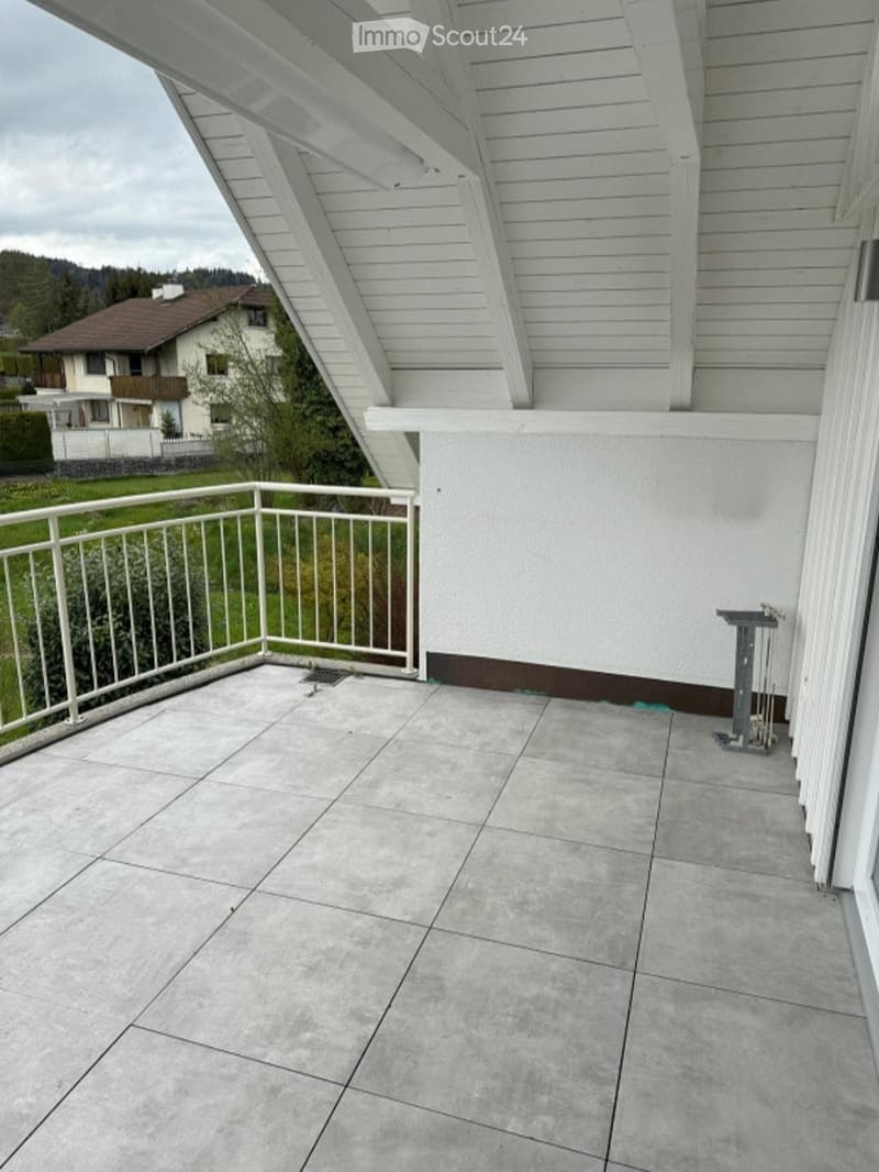 Balcony with grey tiled floor, white metal railing, and a small table with chairs in the corner.