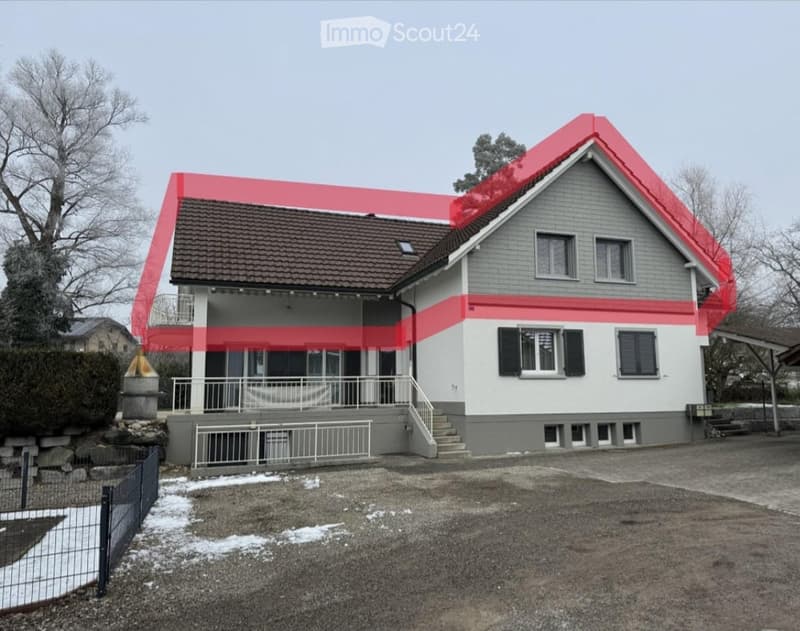 Two-story house with a gray exterior, red roof accents, and a covered porch area. The house features multiple windows with shutters and a small staircase leading to the entrance.