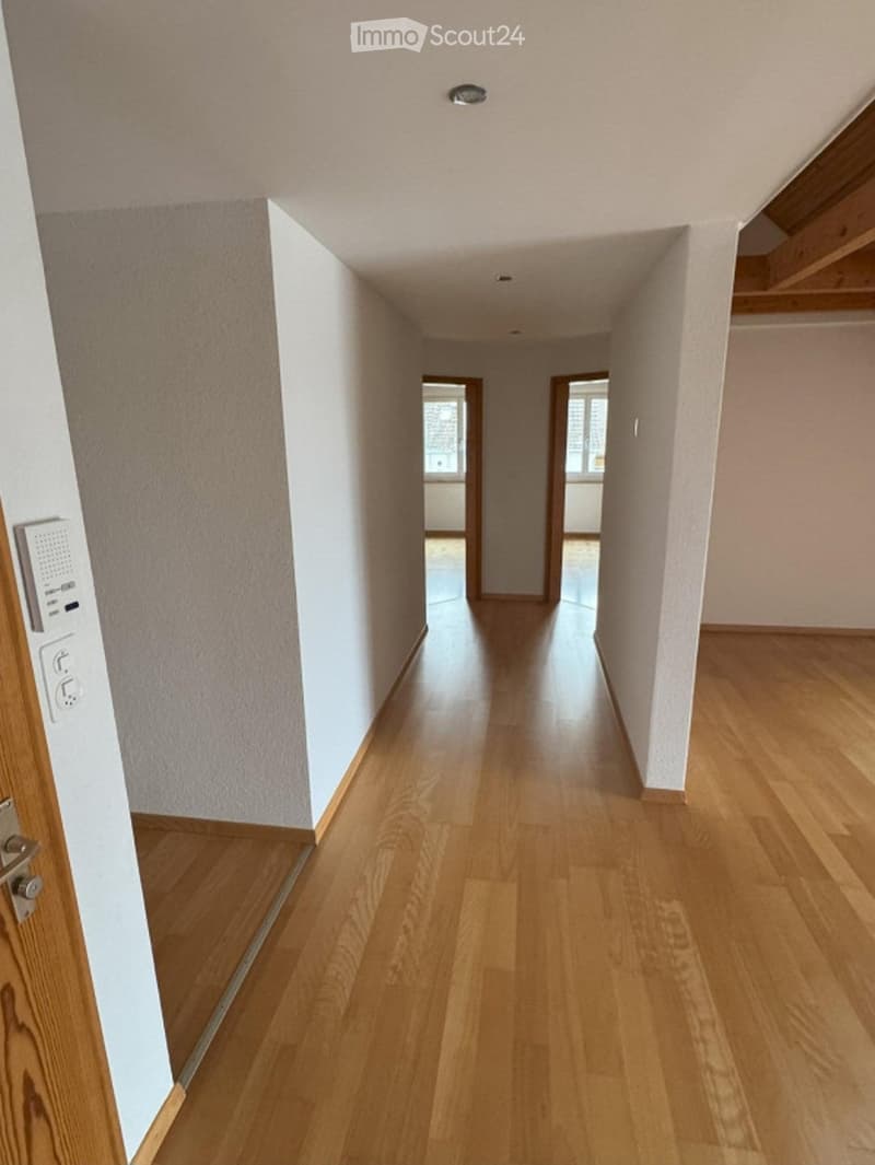 Empty hallway with light wooden flooring, white walls, and recessed ceiling lighting. Doors lead to adjacent rooms.