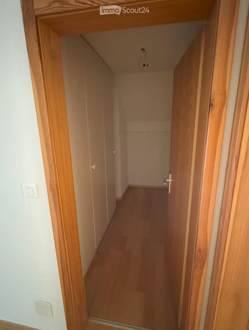 Empty hallway with wooden flooring and white walls, featuring a visible electrical outlet and a partially open door at the end.
