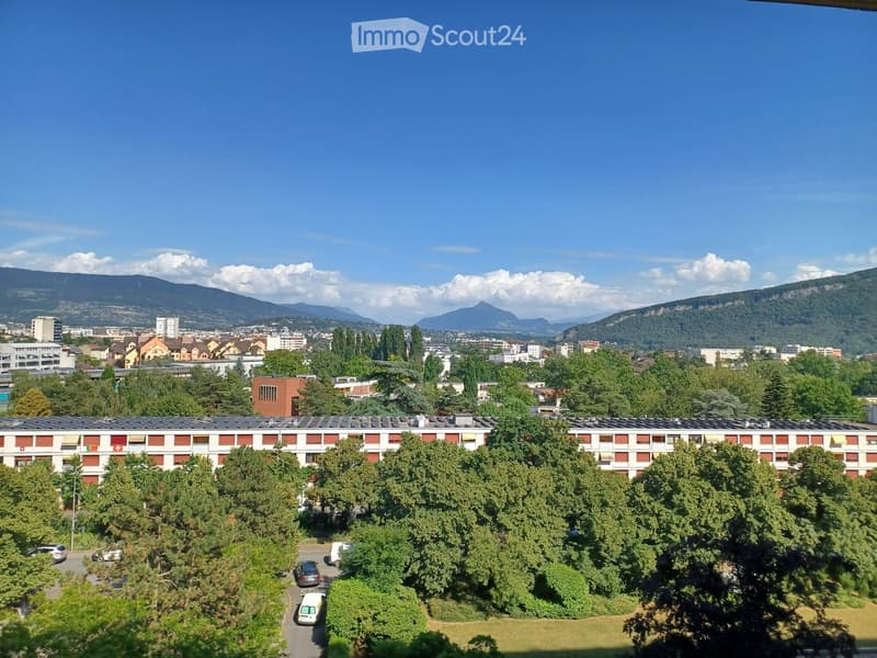 A multi-story residential building with red and white facade, surrounded by trees and parked cars, with a cityscape and mountains in the background.