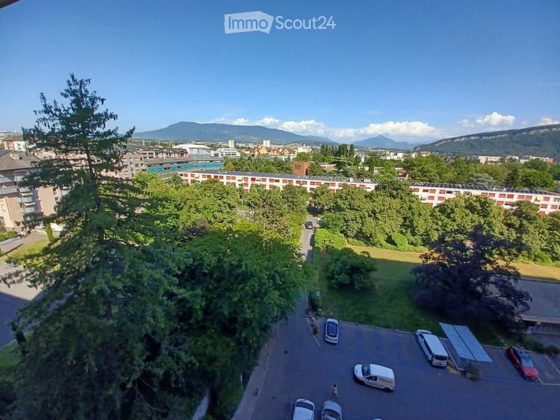 Aerial view of a residential area with a parking lot, trees, and distant mountains under a clear blue sky.