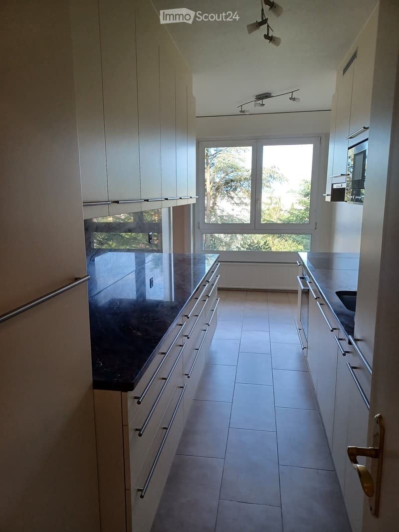 Modern hallway with white tiled flooring, white walls, and built-in cabinets with silver handles. Features a large window at the end, allowing natural light to enter.